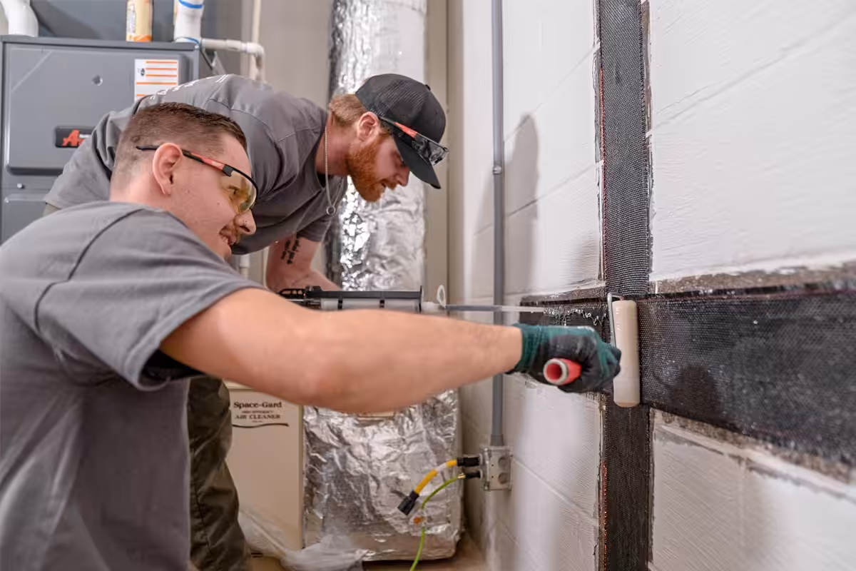 Foundation team applying epoxy on carbon fiber straps in a basement