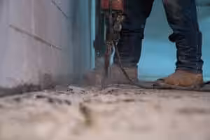 A man using a jackhammer to break up concrete in a basement