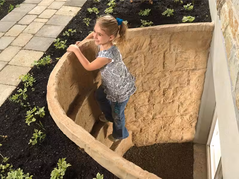 A young girl climbing up a basement egress window escape well