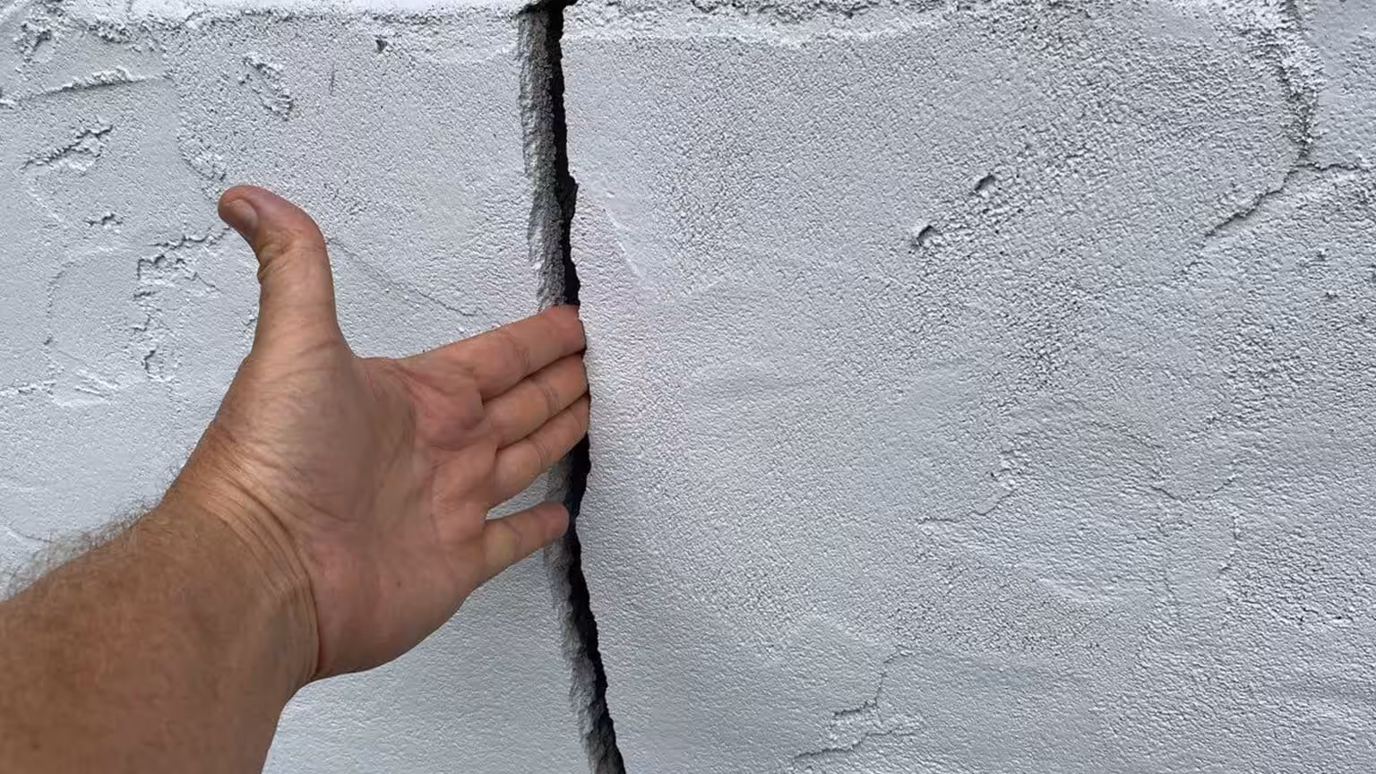 A man's hand fitting inside a foundation wall crack of a home
