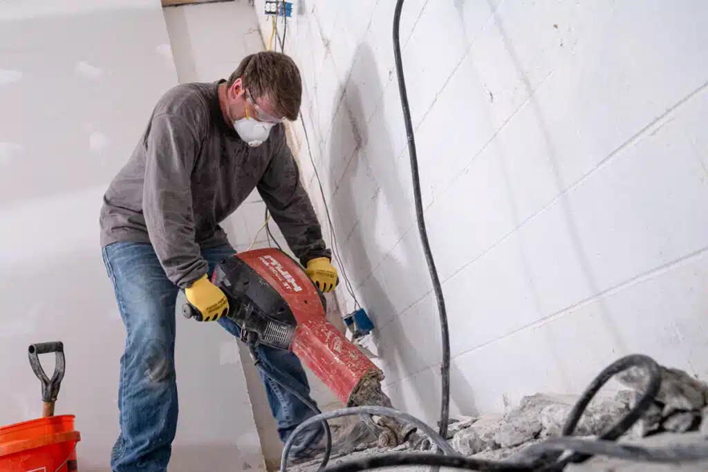 Employee jackhammering a trench for basement waterproofing solutions